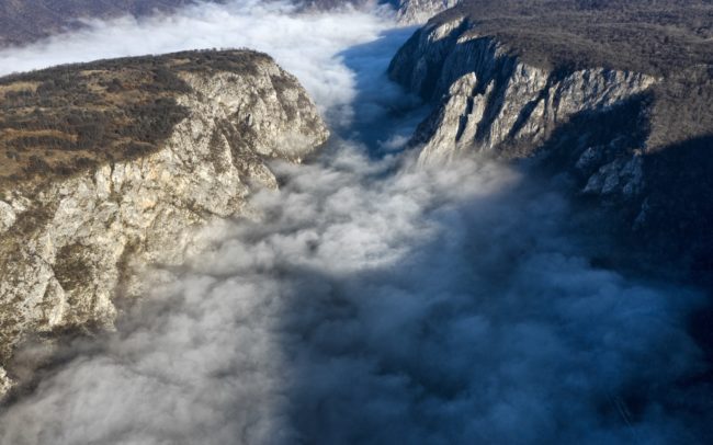 A Duna Szerbia és Románia között. Itt, a szerb oldalon a Djerdap Nemzeti Park terül el partján, szemben pedig a romániai Vaskapu Természetvédelmi terület. Közismertebb nevein ez a hely a Vaskapu vagy Kazán-szoros. A két ország mezsgyéjén, Európa leghosszabb szurdokában szűkül össze az addigra hatalmasra duzzadt folyam. Az első reggelen sikerült megörökíteni a folyót, de a másodjára a köd keresztülhúzta a számításaimat. Viszont teremtett egy teljesen új helyzetet. Így lett nevéhez méltó a hely. Ott, valahol a gomolygó füstszerű köd alatt kavarog, kanyarog titokzatosan a vad víz, mint egy üstben, katlanban. A meredek mészkő sziklafalak 150 méternyire szűkítik, cserébe ezért viszont 82 méter mély a víz- ez a világ legnagyobb folyómélysége.